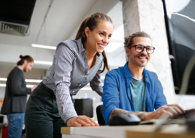 Eine Frau und ein Mann schauen auf einen Monitor.